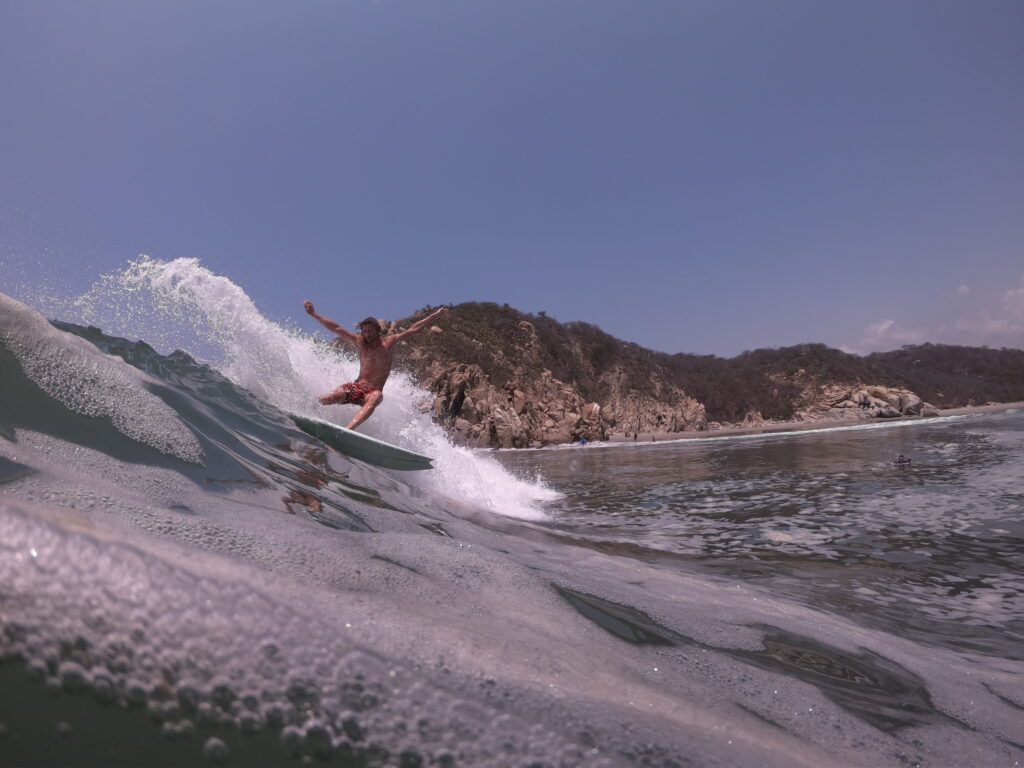 Surfer riding a long wave at Barra with stunning cliffs in the background and clear waters at sunrise