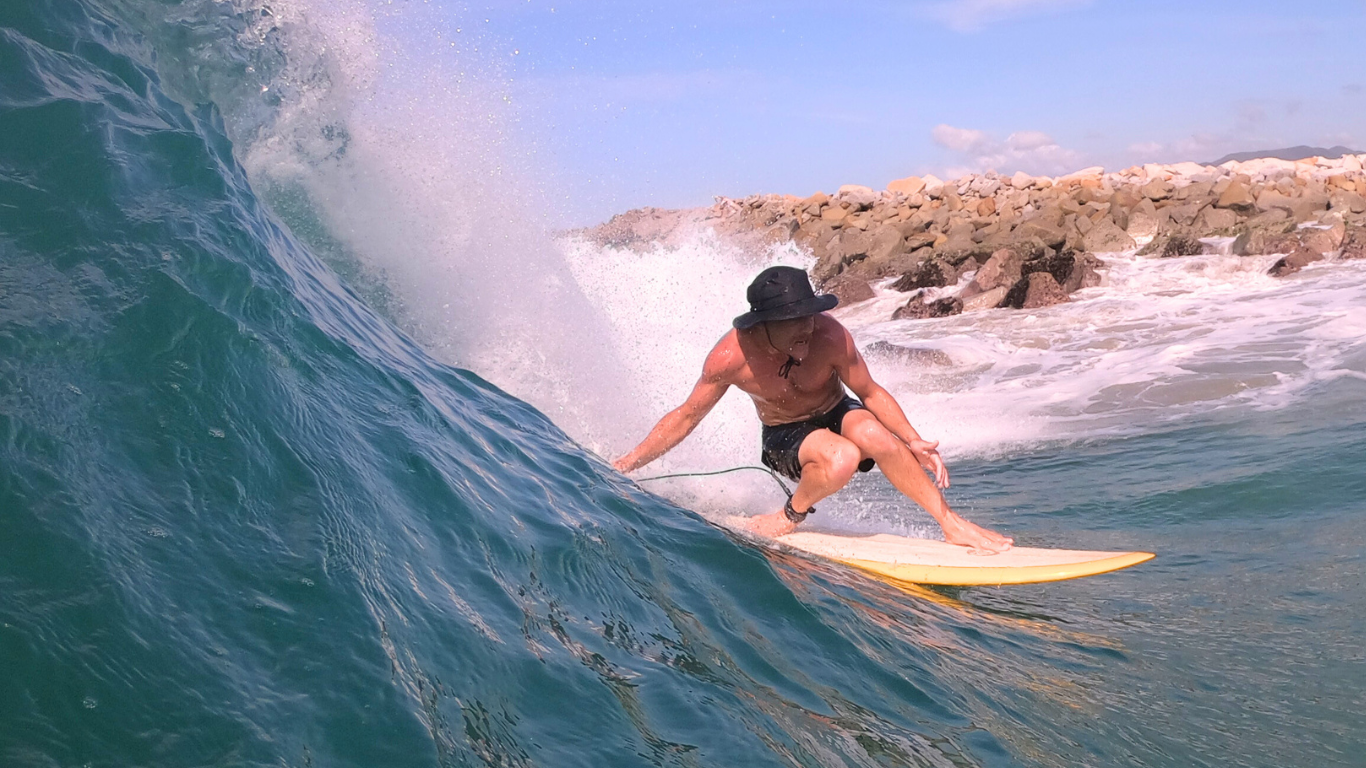 "A surfer carving through a large, crystal-clear wave in Salina Cruz, Oaxaca, with dramatic coastal cliffs and tropical jungle in the background."