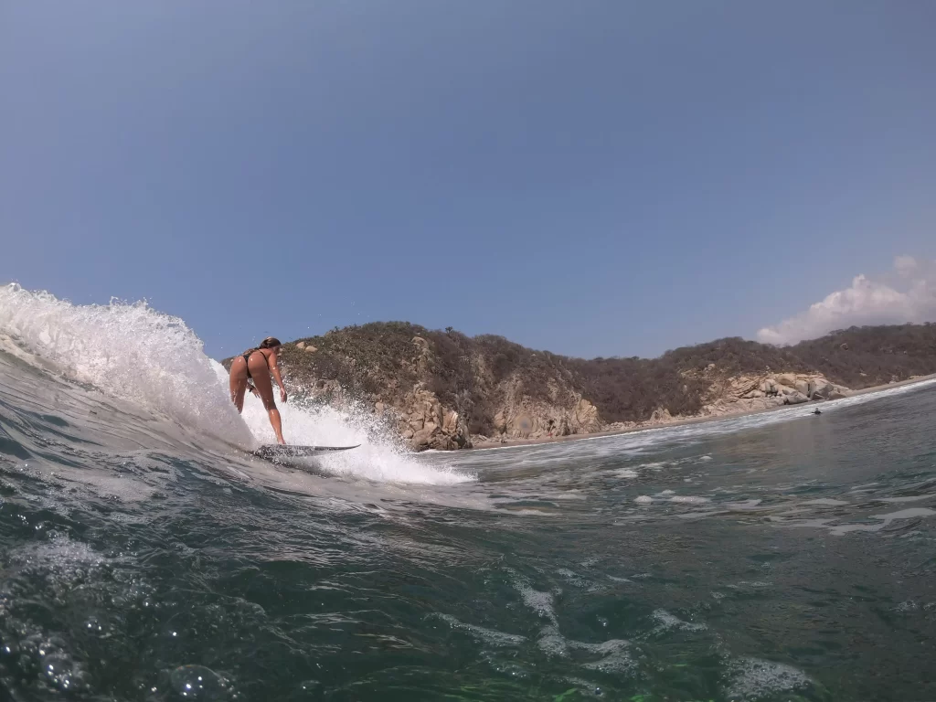 Surfer riding a wave in one of Huatulco’s secluded, uncrowded beaches, with lush green hills in the background